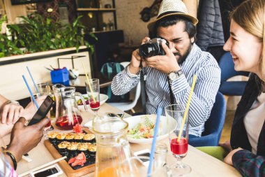 Bir grup neşeli genç arkadaş bir kafede oturuyor, yemek yiyor, içki içiyor. Arkadaşlar selfie çeker ve fotoğraf çeker..
