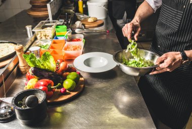 Oteldeki mutfak restoranında yemek pişiren profesyonel bir aşçı. Yemek hazırlıyor. Önlüklü bir aşçı sebze ve pizzadan salata yapar..