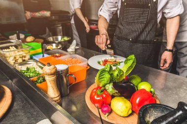 Oteldeki mutfak restoranında yemek pişiren profesyonel bir aşçı. Yemek hazırlıyor. Önlüklü bir aşçı sebze ve pizzadan salata yapar..