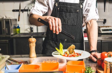 Oteldeki mutfak restoranında yemek pişiren profesyonel bir aşçı. Yemek hazırlıyor. Önlüklü bir aşçı sebze ve pizzadan salata yapar..