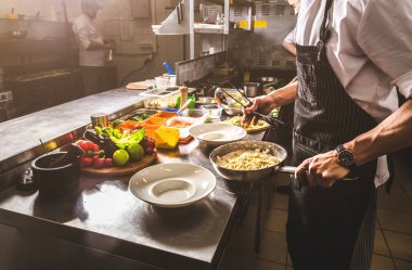 Oteldeki mutfak restoranında yemek pişiren profesyonel bir aşçı. Yemek hazırlıyor. Önlüklü bir aşçı sebze ve pizzadan salata yapar..