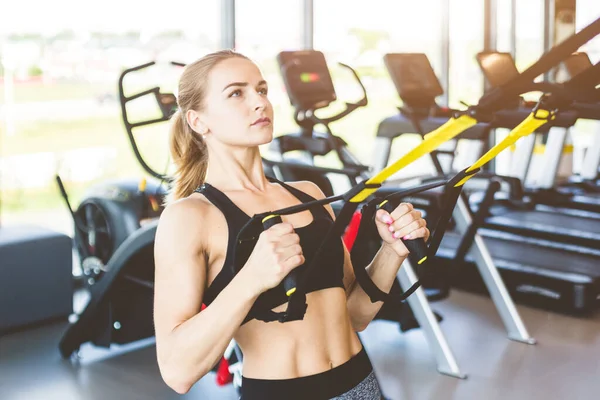 Entrenamiento de mujeres con correas de fitness en el gimnasio. Hermosa dama ejercitando sus músculos honda o correas de suspensión. — Foto de Stock