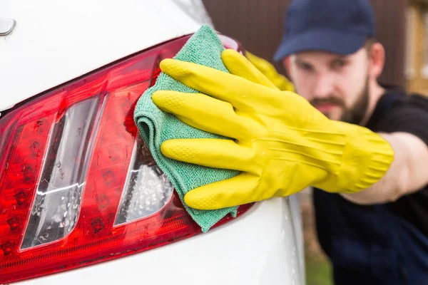 Städning. Man i uniform och gula handskar tvättar en bilkropp i en biltvätt — Stockfoto