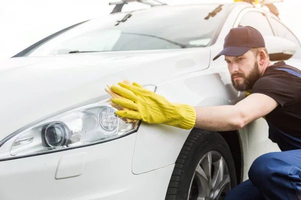 Servicio de limpieza. El hombre de uniforme y guantes amarillos lava una carrocería en un lavado de autos — Foto de Stock