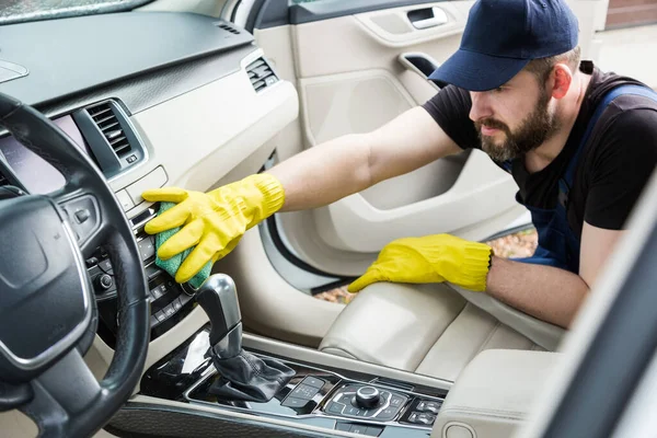 Städning. Man i uniform och gula handskar tvättar en bil interiör i en biltvätt — Stockfoto