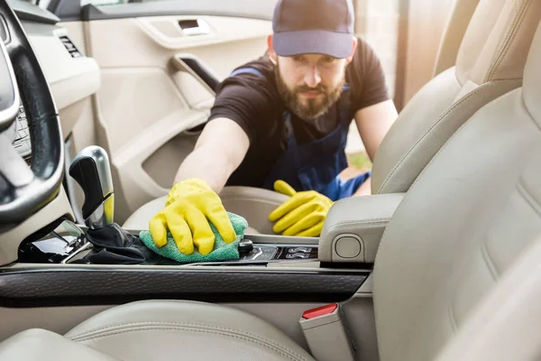 Städning. Man i uniform och gula handskar tvättar en bil interiör i en biltvätt. Arbetaren tvättar stolarna i lädersalongen — Stockfoto