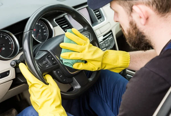 Städning. Man i uniform och gula handskar tvättar en bil interiör i en biltvätt — Stockfoto