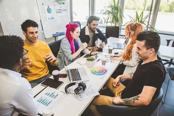 Grupo de ejecutivos multiétnicos discutiendo durante una reunión. Hombre y mujer de negocios sentados alrededor de la mesa en la oficina y sonriendo. Un equipo de jóvenes diseñadores creativos — Foto de Stock