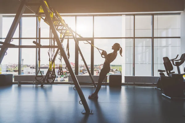 Entrenamiento de mujeres con correas de fitness en el gimnasio. Hermosa dama ejercitando sus músculos honda o correas de suspensión. — Foto de Stock