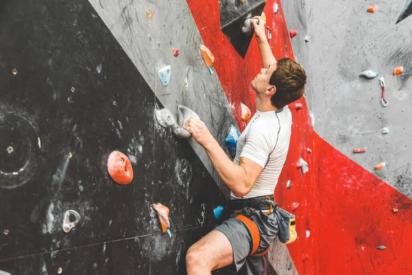 Deportista escalador ascendiendo en roca escarpada, escalando en la pared artificial en el interior. Concepto de deportes extremos y bouldering — Foto de Stock