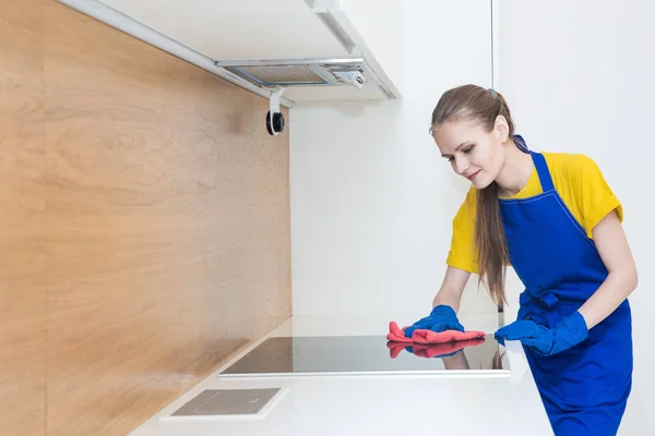 Serviço de limpeza profissional. Duas mulheres em uniforme de trabalho, em aventais, dividir a limpeza da cozinha de uma casa particular, casa de campo. lavar a geladeira, torneira, pia. Lavar o chão. — Fotografia de Stock