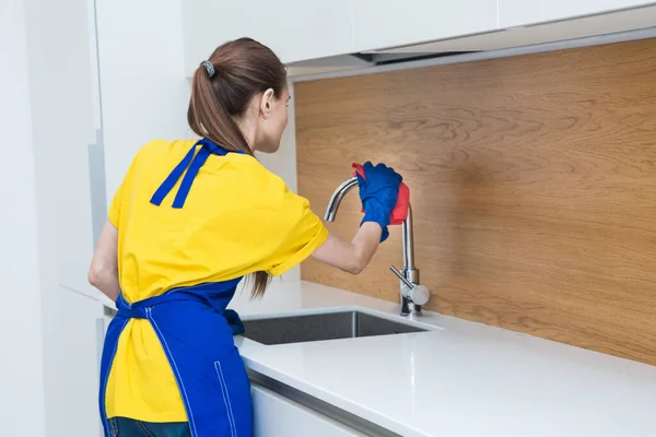 Servicio de limpieza profesional. Dos mujeres en uniforme de trabajo, en delantales, dividen la limpieza de la cocina de una casa privada, casa de campo. lavar el refrigerador, grifo, fregadero. Lavar el suelo. —  Fotos de Stock