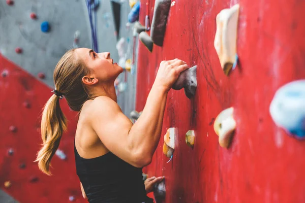 Deportiva escaladora ascendiendo sobre roca escarpada, escalando en pared artificial en interiores. Concepto de deportes extremos y bouldering — Foto de Stock