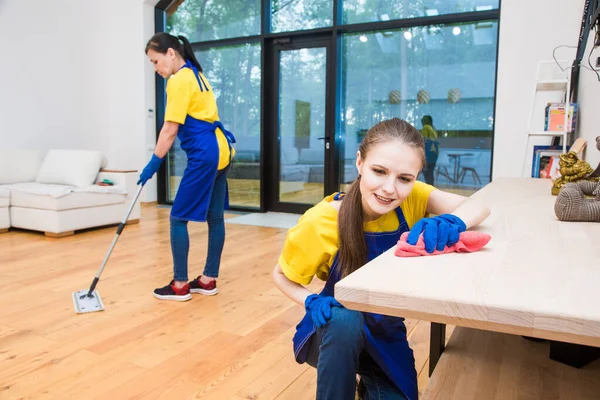 Servicio de limpieza profesional. Dos mujeres en uniforme de trabajo, en delantales, dividen la limpieza de la cocina de una casa privada, casa de campo. Suelo de lavado —  Fotos de Stock