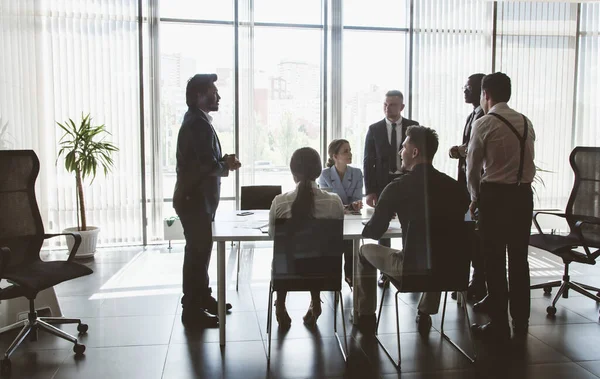 Siluetas de gente sentada a la mesa. Un equipo de jóvenes empresarios que trabajan y se comunican en una oficina. Corporativossteam y gerente en una reunión — Foto de Stock