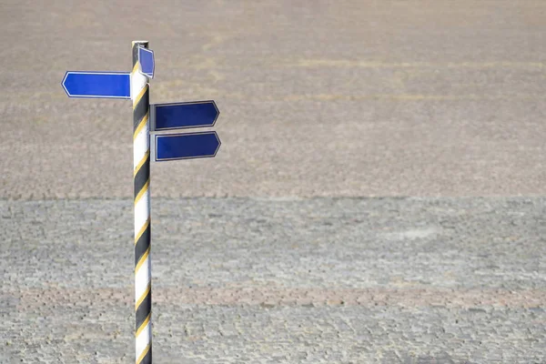 Striped roadsign with blank direction arrows against stone pavement