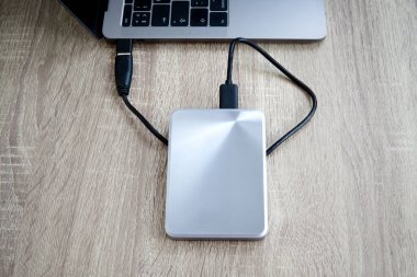 Taşınabilir sabit disk, tahta bir masadaki dizüstü bilgisayara bağlı. Bir dizüstü bilgisayar ve sabit disk arasında veri transferi veya yedekleme.