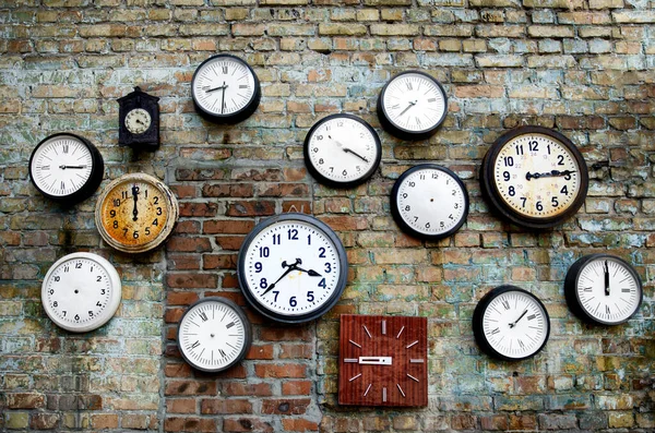 许多不同尺码的老式时钟挂在一面磨擦的砖墙上 圆形和正方形的时钟显示出不同的时间 有些钟是没有指针的 — 图库照片