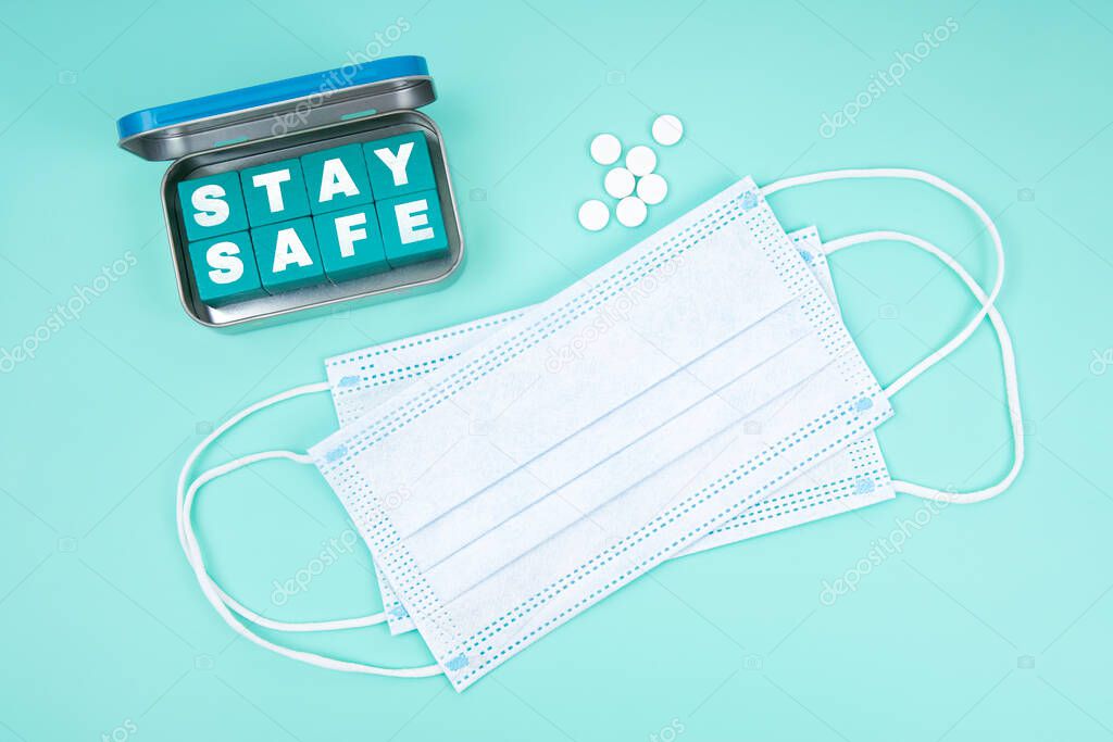 Disposable face masks, pills and a steel box with wooden letter cubes spelling STAY SAFE text conveying a message to take care and observe preventive measures to control the virus outbreak.