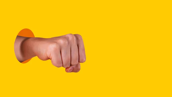 Womans hand fist from hole. Yellow background.