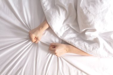 Kadın elleri kar beyazı çarşafı kavrıyor.