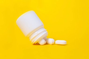 Plastik ilaç kavanozundan düşen beyaz haplar. Parlak sarı arkaplan. Minimalist tıp ve sağlık hizmeti konsepti. Eczacılık ilaçları, haplar. Kapat şunu..