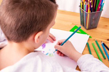 İzolasyonda pastel boyalarla resim çizen tanınmamış beyaz çocuk. Ahşap masa arkaplanı.