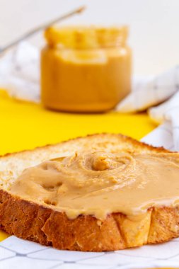 Kızarmış ekmeğin üzerinde fıstık ezmeli sandviç iştah açıcı. Arka planda bir kavanoz dolusu fıstık ezmesi. Sarı arka plan ve beyaz peçete. Seçici odak.