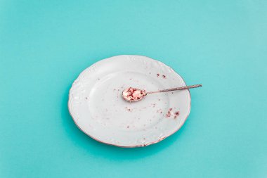 Boş beyaz tatlı tabağı ve mavi arka planda çay kaşığı. Biri pasta ve tatlı yemiş. Yıkanmamış tabak. Arta kalanlar..