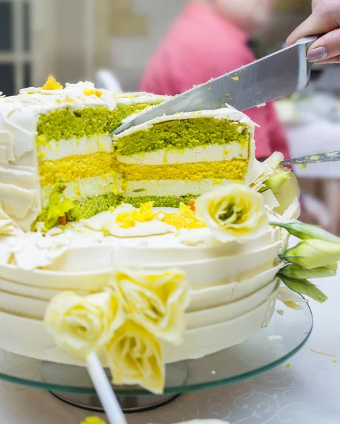 Sliced bride cake with flowers and yellow green cakes.