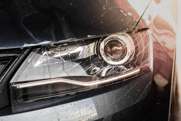 Gocce d'acqua e schiuma sulla luce dell'auto nella stazione di lavaggio vele. Pulizia concetto di automobile, inquinamento delle acque sotterranee . — Foto Stock