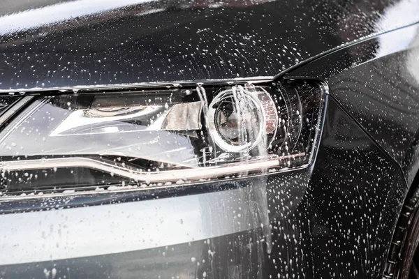 Gocce d'acqua e schiuma sulla luce dell'auto nella stazione di lavaggio vele. Pulizia concetto di automobile, inquinamento delle acque sotterranee . — Foto Stock