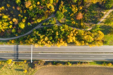 Sonbahar ormanı ve ekilmiş toprak arasında sonbaharda günbatımında sarı ağaçlar. Yarış pistindeki trafiğin havadan görüntüsü
