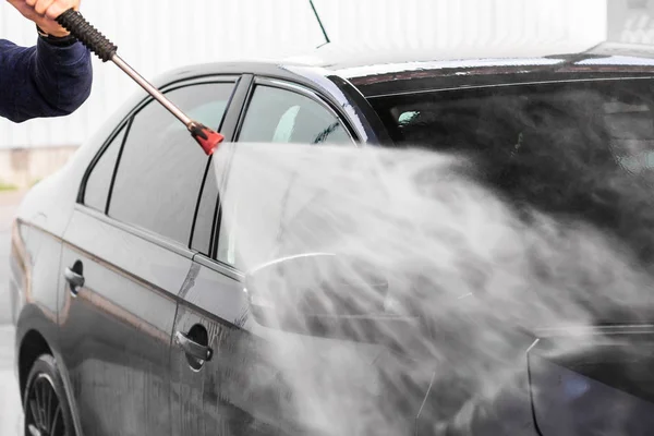 Een man wast een auto bij autowasserij, hogedrukreiniger schoon met water. Autowasmachines — Stockfoto