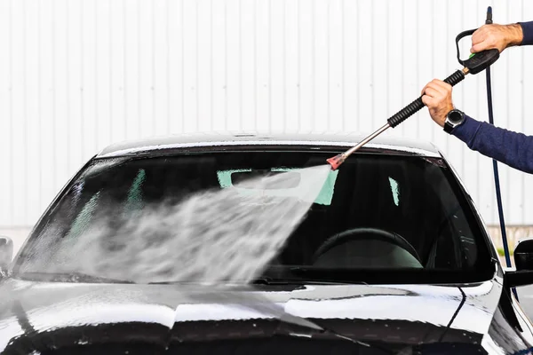 Mężczyzna myje samochód w myjni samoobsługowej. Wysokie ciśnienie pojazdu pralka czysta wodą. Urządzenia do mycia samochodów — Zdjęcie stockowe