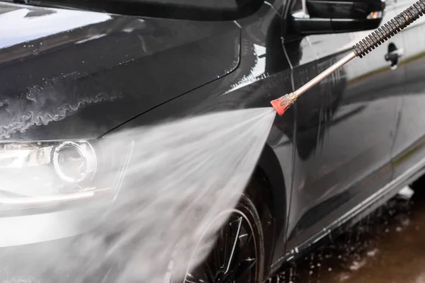 Egy férfi kocsit mos az önkiszolgáló autómosóban, nagy nyomású mosógéppel, vízzel tisztára mosva. Autómosó berendezés — Stock Fotó