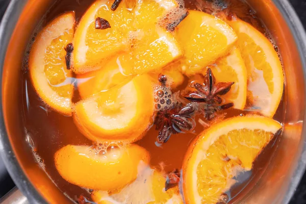 Making hot alcoholic mulled wine with oranges and spices. Christmas beverages boil in the metal pan. Glintwine from rose wine with citrus, cloves, star anise, cinnamon.