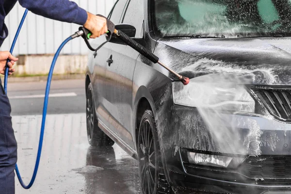 Muž myje auto v samoobslužné myčce aut. Vysokotlaká myčka vozidel rozstřikuje pěnu. Mladá Boleslav, 10.12.2019 — Stock fotografie