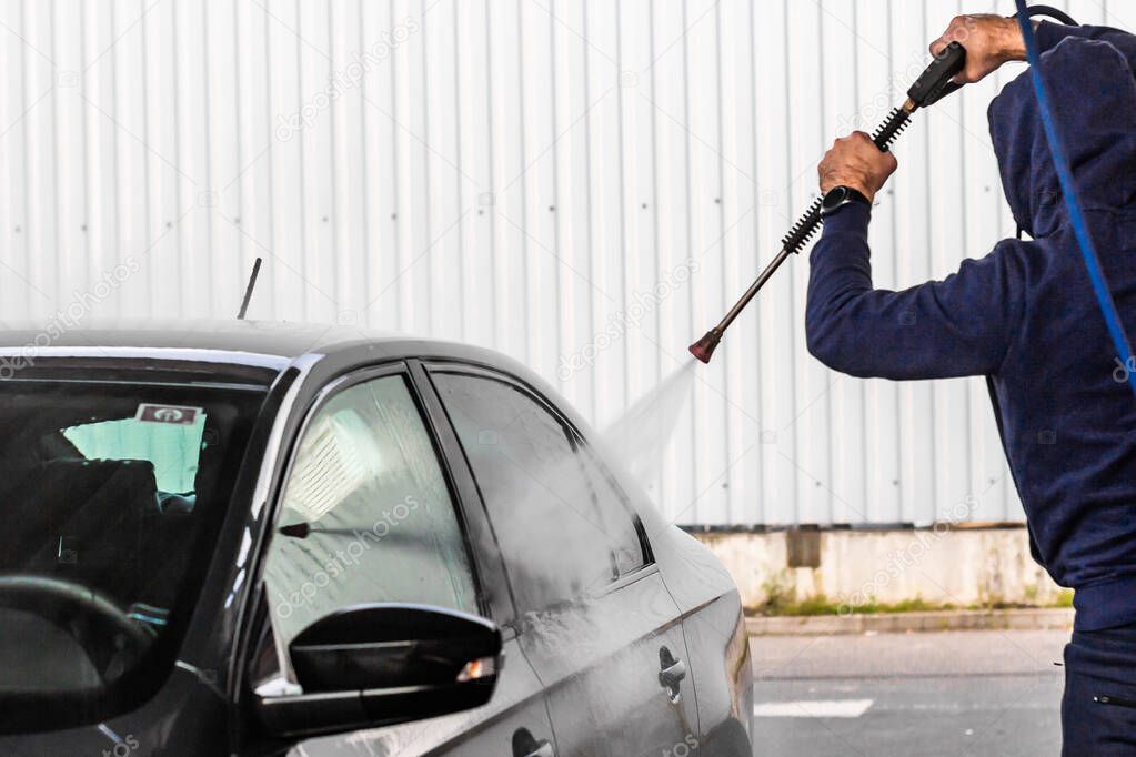 A man is washing a car at self service car wash. High pressure vehicle washer machine clean with water. Car wash equipment, Mlada Boleslav, 10.12.2019