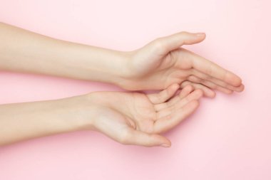 Kadın ellerini pembe arka planda tutuyor. Hassas cilt bakımı için kozmetik ürünleri. Doğal kozmetik ürünleri, kırışıklık önleyici el bakımı. İnce bir bilek ve doğal manikür..
