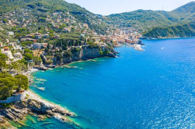 Aerial view on the city with colorful houses located on the rocky coast of ligurian sea, Camogli near Genoa, Italy. Rocky Coastline is washed by turquoise blue water.