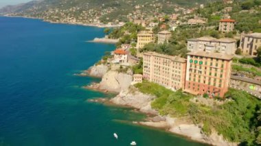 Turkuaz mavi deniz suyunun altında kocaman taşlarla deniz kıyısına uç. İtalya 'nın Cenova kenti yakınlarında geleneksel renkli evleri olan Camogli kenti.