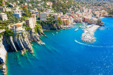 Marina and breakwater where lighthouse is located. Boat sailing to the harbor in ligurian sea, Camogli near Portofino, Italy. Aerial view on traditional Italian colorful houses