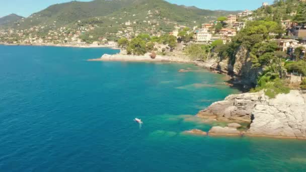 一艘小船正从意大利热那亚附近的卡莫格利港驶出。一艘汽艇正沿着岩石海岸驶回码头. — 图库视频影像