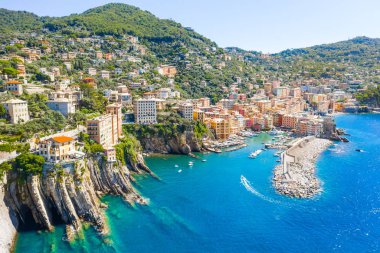 Marina and breakwater where lighthouse is located. Boat sailing to the harbor in ligurian sea, Camogli near Portofino, Italy. Aerial view on traditional Italian colorful houses
