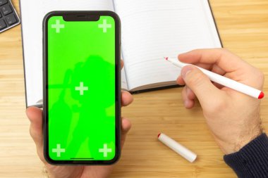 Ofis masasının üzerinde yeşil ekranlı siyah cep telefonu ve kırtasiye araçlarıyla kırmızı çizgili el kamerası görüntüsü. San Francisco, Şubat 2020