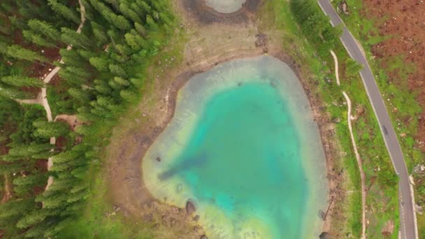 Vue aérienne de l'eau turquoise bleue du lac Carezza dans les Dolomites des Alpes. Survolez Lago di Karersee près d'une forêt de sapins . — Video