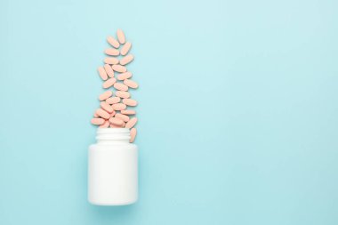 Mavi arka planda şişeden serpilmiş vitamin hapları. Çocuklar için ilaç reklamı kavramı.