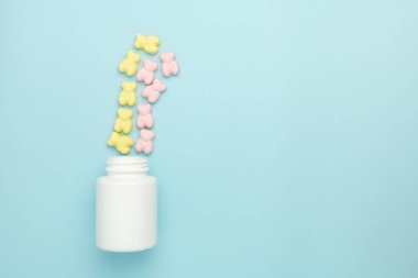 Jöle peluş ayı vitamin sakızları mavi arka planda şişeden serpilmiş. Çocuklar için ilaç reklamı kavramı.