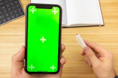 Ofis masasının üzerinde yeşil ekranlı siyah cep telefonu ve kırtasiye araçlarıyla kırmızı çizgili el kamerası görüntüsü. San Francisco, Şubat 2020